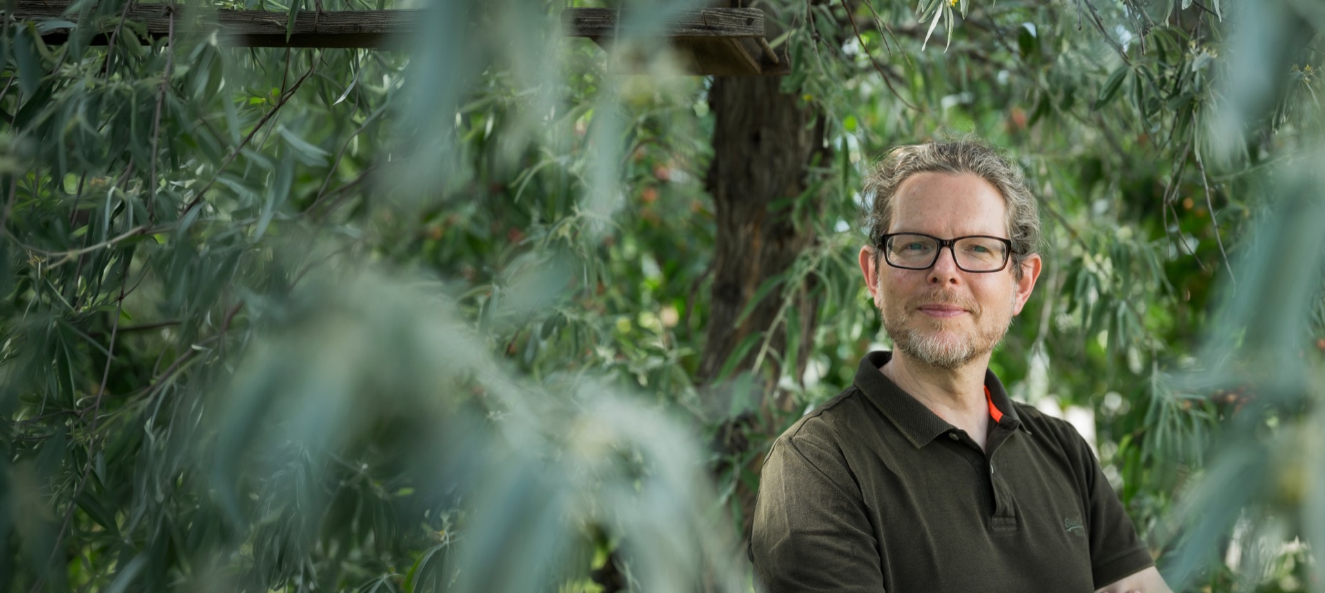 Lorenz Papis, lächelnd zwischen grünen Weidenzweigen im Garten