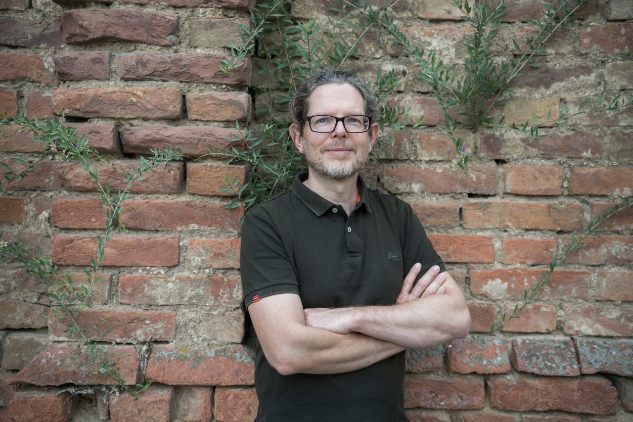 Lorenz Papis mit verschränkten Armen vor einer Ziegelmauer
